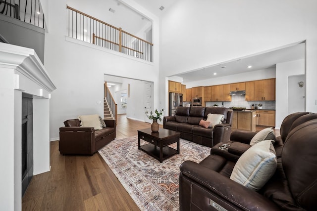 living room with stairway, dark wood-type flooring, a towering ceiling, baseboards, and a fireplace