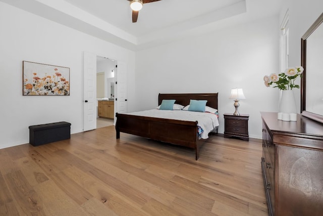 bedroom with light wood-style floors, a tray ceiling, ensuite bathroom, and baseboards