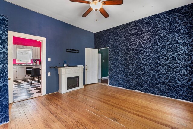 523 Ash St, Lockhart, TX 78644 - unfurnished living room with a sink, a ceiling fan, a fireplace, wallpapered walls, and wood-type flooring