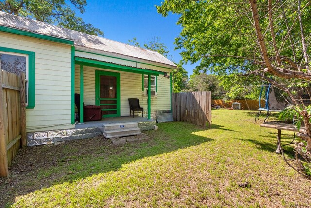 523 Ash St, Lockhart, TX 78644 - rear view of property featuring a trampoline, a yard, metal roof, fence, and covered porch