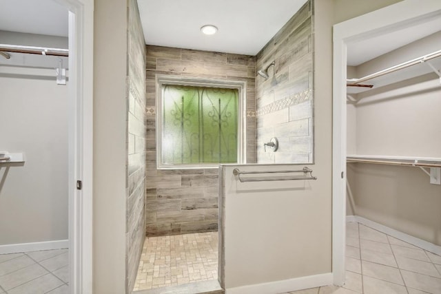 bathroom with a walk in shower, tile patterned flooring, a spacious closet, and baseboards