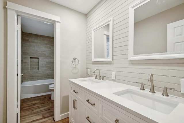 full bathroom with toilet, wood finished floors, double vanity, and a sink