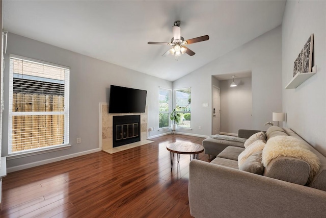 living area with wood finished floors, vaulted ceiling, a tiled fireplace, a ceiling fan, and baseboards