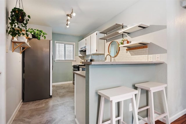 kitchen featuring freestanding refrigerator, tasteful backsplash, baseboards, a kitchen breakfast bar, and white cabinets
