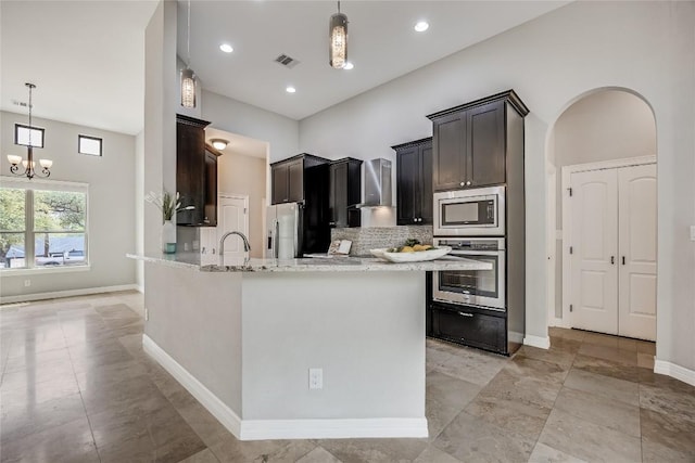 21434 Lakefront Dr, Lago Vista, TX 78645 - kitchen with appliances with stainless steel finishes, wall chimney range hood, tasteful backsplash, light stone counters, and a chandelier