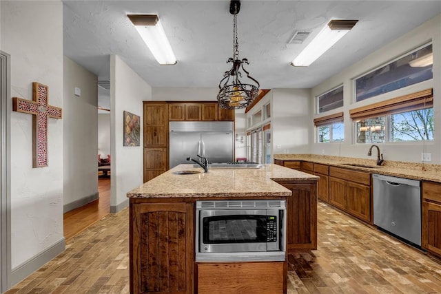 202 Bridgepoint Dr, Kingsland, TX 78639 - kitchen with built in appliances, a sink, light wood finished floors, a kitchen island with sink, and brown cabinets