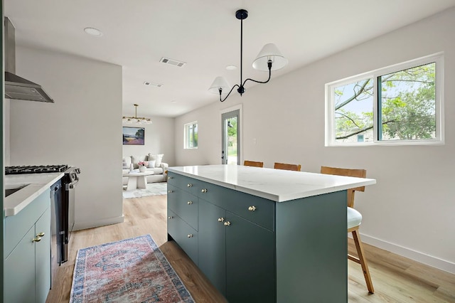 7614 Watson St, Austin, TX 78757 - kitchen featuring wall chimney range hood, light wood-style floors, a kitchen island, a breakfast bar area, and recessed lighting