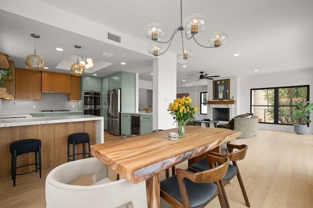4328 Far W Blvd, Austin, TX 78731 - dining space featuring a fireplace, beverage cooler, light wood-style flooring, ceiling fan with notable chandelier, and visible vents