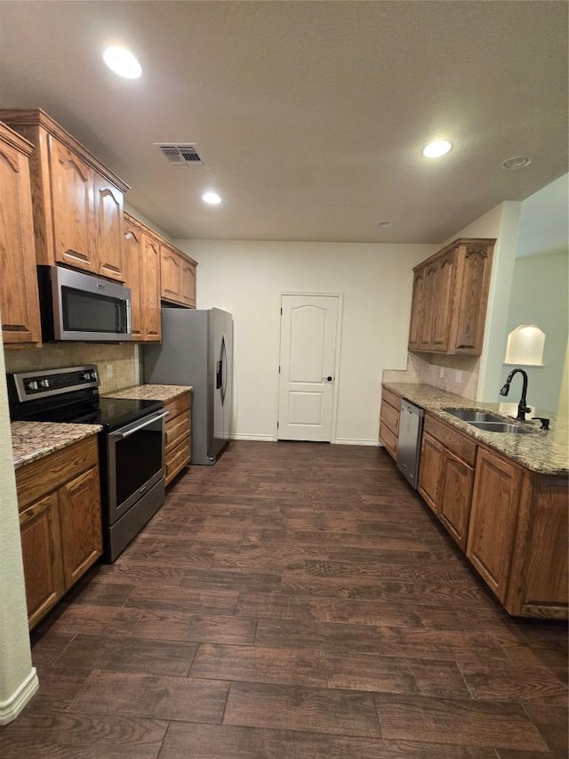 kitchen featuring light stone countertops, a sink, tasteful backsplash, dark wood-type flooring, and appliances with stainless steel finishes