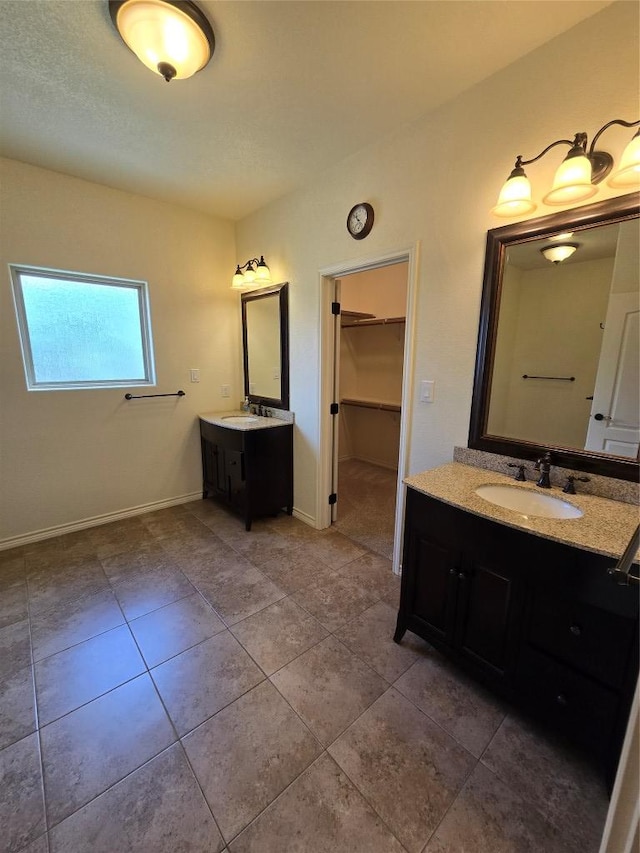 full bathroom featuring a walk in closet, two vanities, a sink, and tile patterned flooring