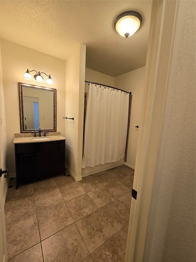 bathroom featuring a textured ceiling, vanity, tile patterned flooring, and baseboards