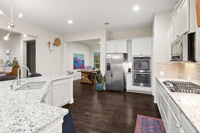 kitchen with a sink, appliances with stainless steel finishes, dark wood-type flooring, decorative backsplash, and white cabinetry