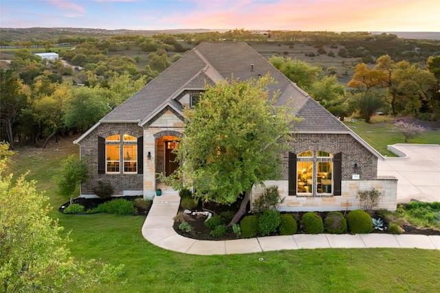 french provincial home with a lawn, brick siding, and stone siding