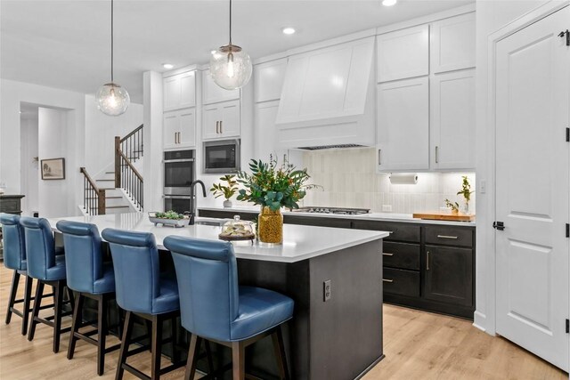 1890 Headwaters Blvd, Dripping Springs, TX 78620 - kitchen with custom exhaust hood, appliances with stainless steel finishes, light countertops, white cabinets, and a kitchen island with sink