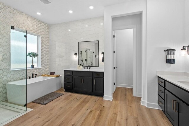 1890 Headwaters Blvd, Dripping Springs, TX 78620 - bathroom featuring two vanities, a shower stall, a soaking tub, wood finished floors, and recessed lighting
