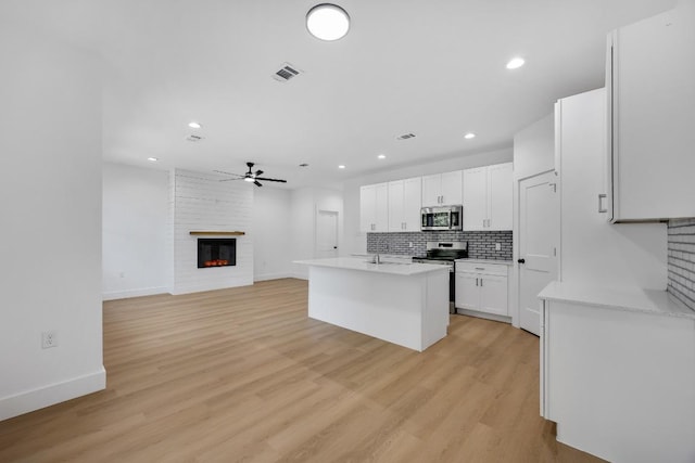 240 Hanauma Dr, Bastrop, TX 78602 - kitchen with appliances with stainless steel finishes, a fireplace, a ceiling fan, white cabinetry, and light countertops