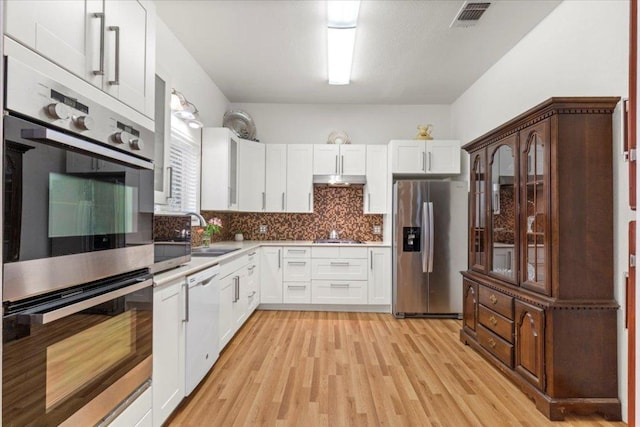 406 Garwood St, Smithville, TX 78957 - kitchen featuring appliances with stainless steel finishes, backsplash, white cabinetry, a sink, and light wood finished floors