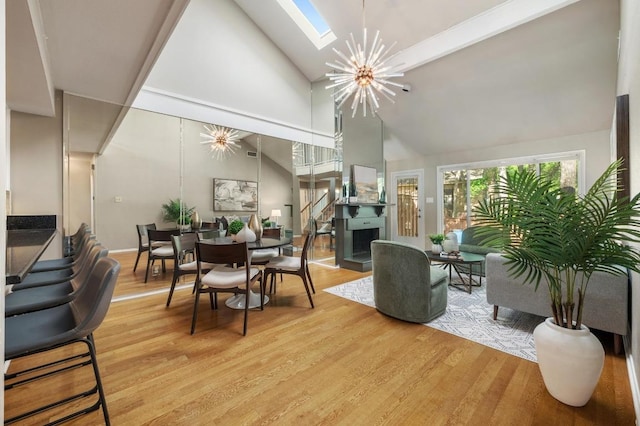 dining space featuring a skylight, a notable chandelier, light wood-style flooring, and high vaulted ceiling
