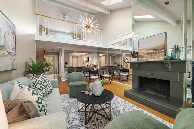 living room featuring a high ceiling, beam ceiling, a fireplace with raised hearth, wood finished floors, and a skylight