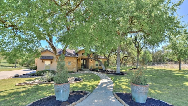 view of front of home with stucco siding, stone siding, fence, and a front lawn