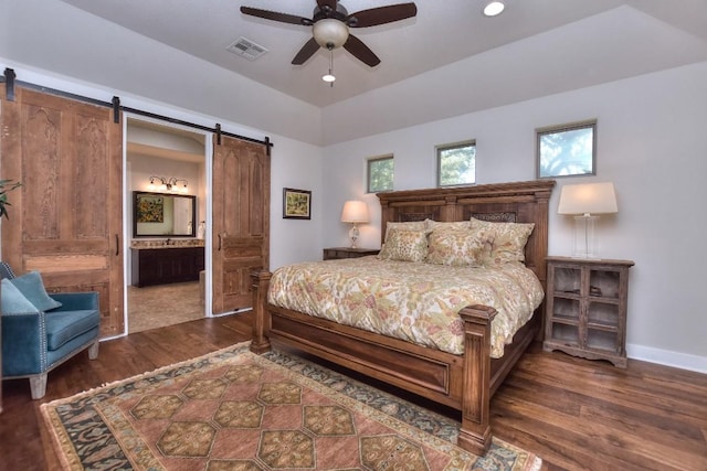 bedroom featuring baseboards, ensuite bathroom, a barn door, visible vents, and wood finished floors