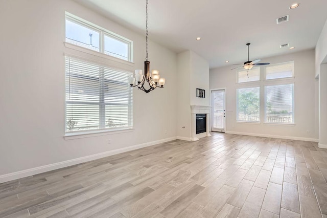 unfurnished living room with light wood-style floors, a healthy amount of sunlight, ceiling fan with notable chandelier, and visible vents