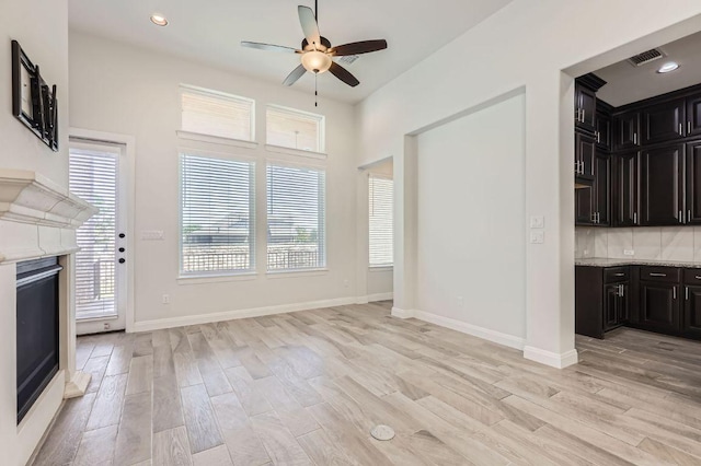 unfurnished living room with ceiling fan, light wood-type flooring, a glass covered fireplace, and baseboards