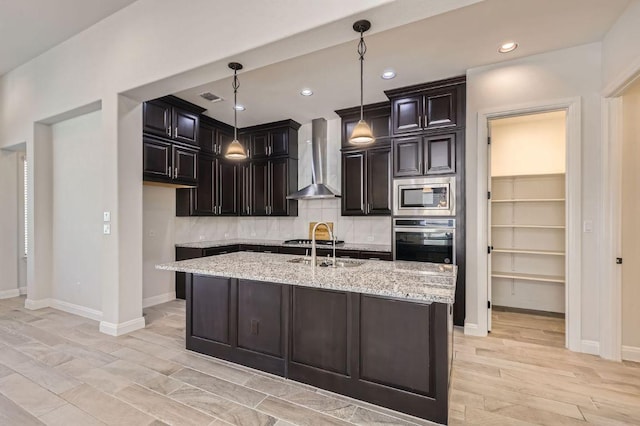 kitchen featuring wall chimney range hood, visible vents, light stone counters, stainless steel appliances, and decorative backsplash