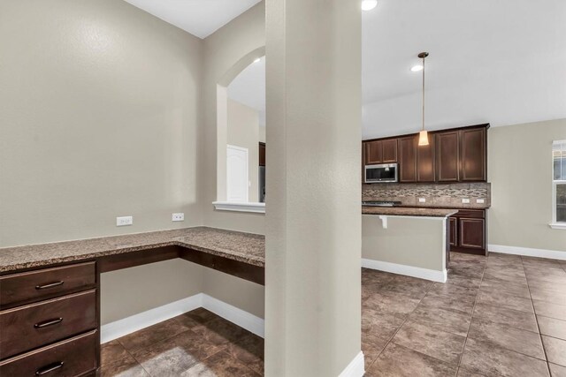 3613 Esperanza Dr, Round Rock, TX 78665 - kitchen featuring stainless steel microwave, dark brown cabinets, arched walkways, backsplash, and baseboards