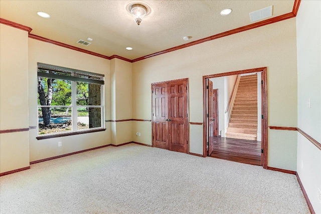 carpeted spare room featuring visible vents, baseboards, and crown molding