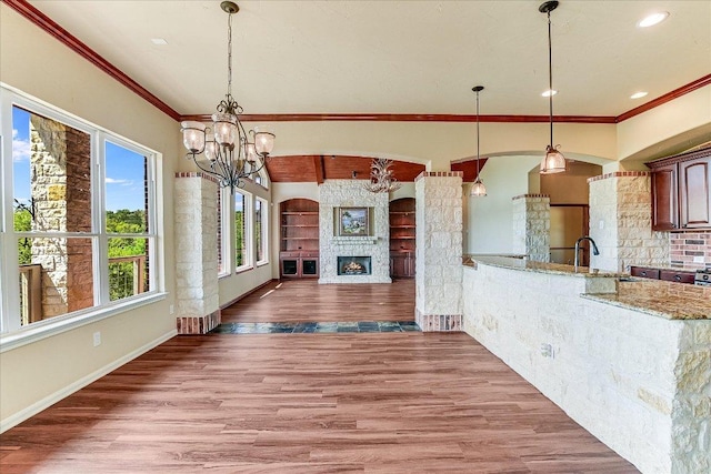 unfurnished dining area with an inviting chandelier, a fireplace, ornamental molding, wood finished floors, and baseboards