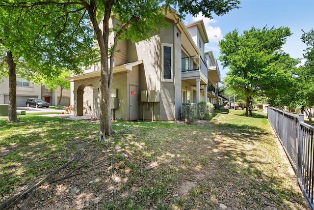 view of side of home featuring a yard, fence, a balcony, and stucco siding