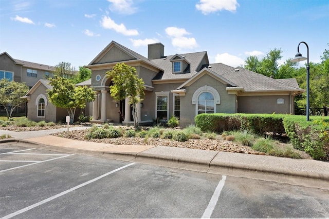 view of front of house featuring uncovered parking, a chimney, and stucco siding