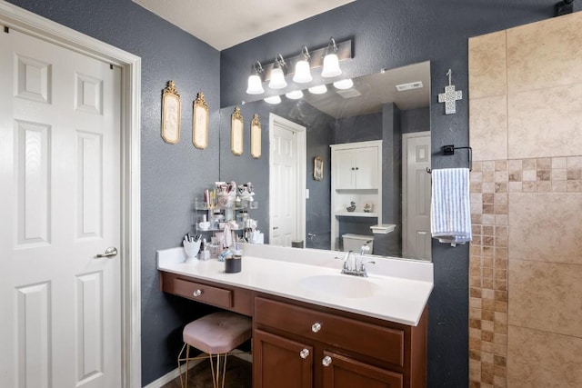 bathroom with toilet, vanity, a textured wall, and visible vents