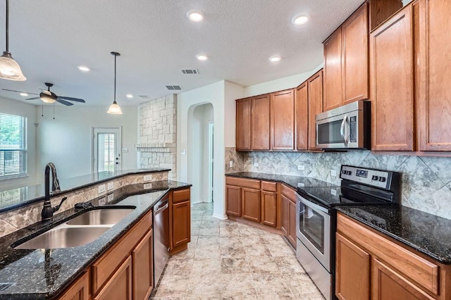 1161 Verna Brooks Way, Kyle, TX 78640 - kitchen featuring appliances with stainless steel finishes, a sink, brown cabinets, hanging light fixtures, and decorative backsplash