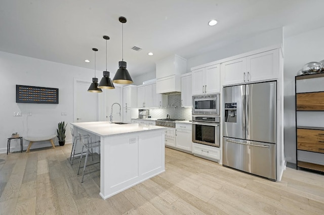 kitchen featuring appliances with stainless steel finishes, decorative backsplash, white cabinetry, light countertops, and light wood-style floors