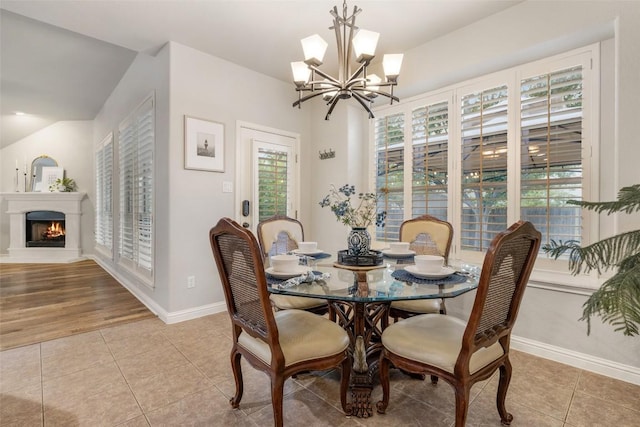 1218 Swenson Farms Blvd, Pflugerville, TX 78660 - dining room featuring a chandelier, vaulted ceiling, light tile patterned flooring, baseboards, and a lit fireplace