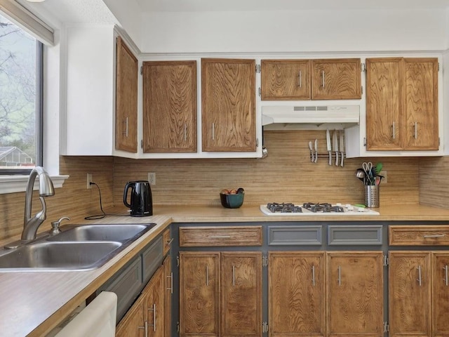 kitchen with a sink, decorative backsplash, under cabinet range hood, white appliances, and light countertops