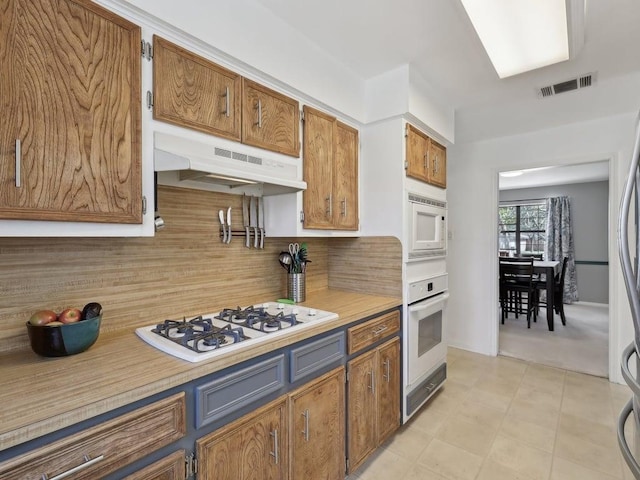 kitchen with tasteful backsplash, white appliances, under cabinet range hood, light countertops, and visible vents