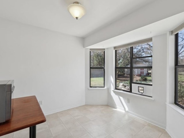 empty room with light tile patterned floors, a healthy amount of sunlight, and baseboards