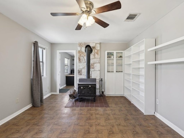 living room with baseboards, visible vents, a ceiling fan, and a wood stove