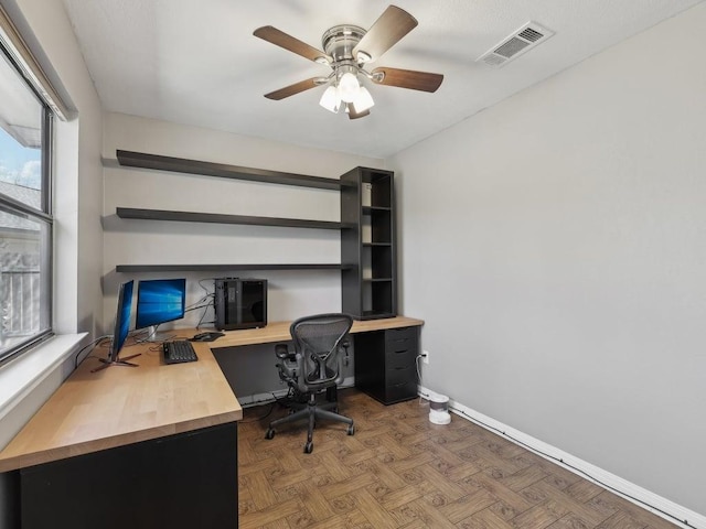 office space with visible vents, a ceiling fan, and baseboards