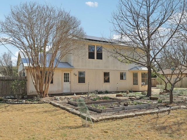 rear view of house with a lawn, a garden, solar panels, and fence