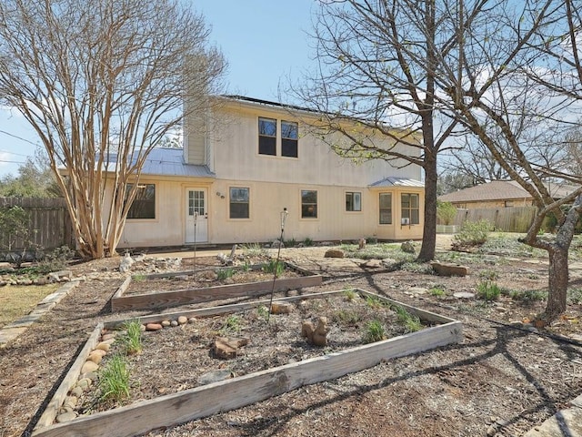 rear view of house featuring fence, a vegetable garden, and metal roof