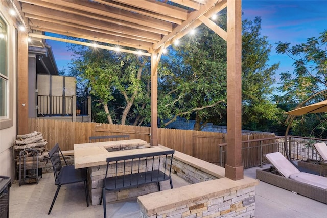 patio terrace at dusk featuring an outdoor fire pit and fence