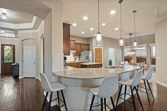 kitchen with arched walkways, stainless steel refrigerator with ice dispenser, a sink, brown cabinetry, and a kitchen island