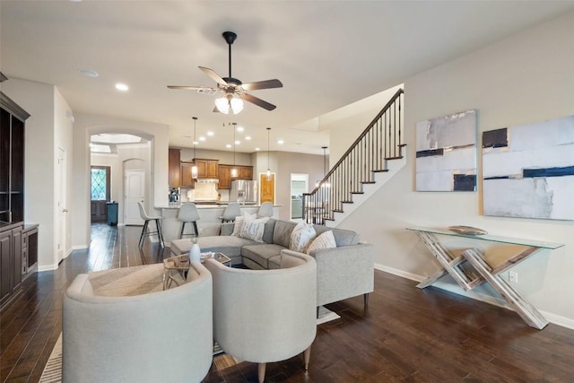 living area with baseboards, arched walkways, ceiling fan, dark wood finished floors, and stairs