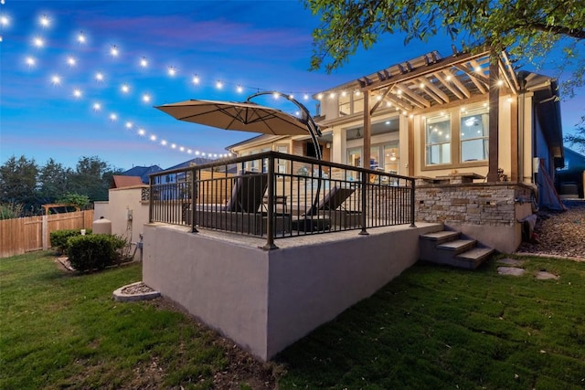 back of house at dusk featuring a yard and fence