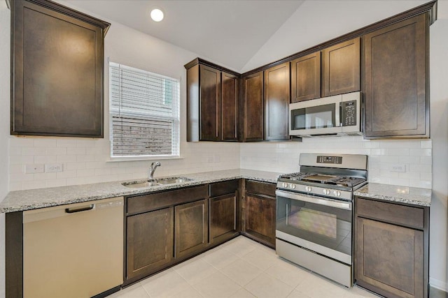 136 Gamble St, Buda, TX 78610 - kitchen with stainless steel appliances, dark brown cabinetry, vaulted ceiling, light stone counters, and tasteful backsplash
