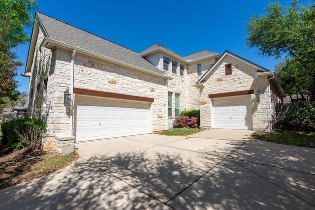 french country inspired facade with a garage, driveway, stone siding, and roof with shingles